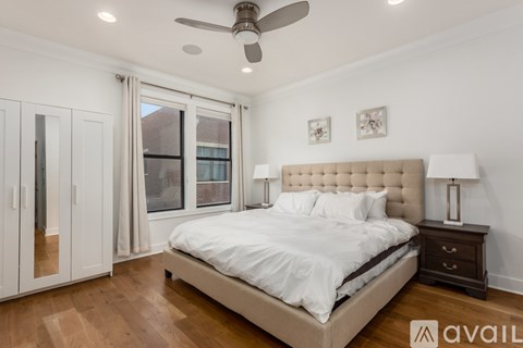 A bedroom with a large bed, a ceiling fan, and a window with a view of a building outside.
