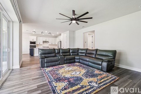 A living room with a black leather sofa and a ceiling fan.