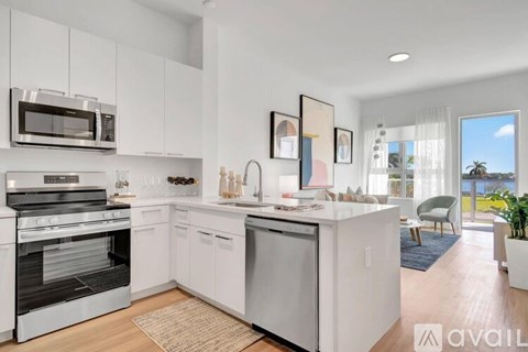 A modern kitchen with white cabinets and appliances, a rug on the floor, and a view of the outdoors through the window.