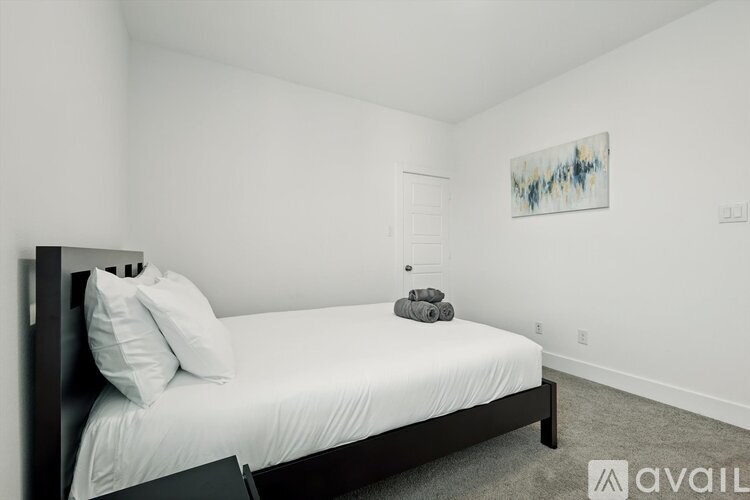 A bedroom with a bed, pillows, and a painting on the wall.
