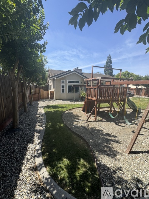 A backyard with a playground and a gravel path.