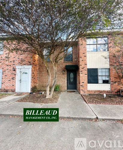 A white car is parked in front of a brick building with a tree in front of the door.