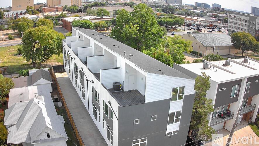 A modern building with a grey and white exterior is surrounded by trees and other buildings.