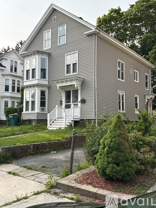 A grey house with a white porch and a green trash can in front.