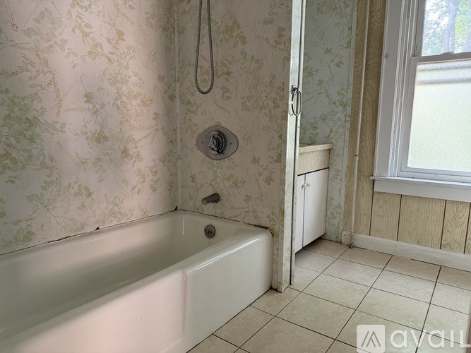 A white bathtub sits in a bathroom with floral wallpaper.