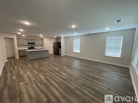 A spacious room with wooden flooring and a kitchen area in the background.