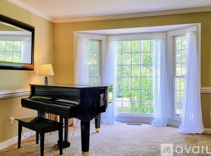 A black grand piano sits in a room with a window and a chair.