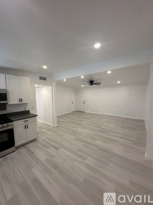 A spacious room with a kitchen area and a ceiling fan.