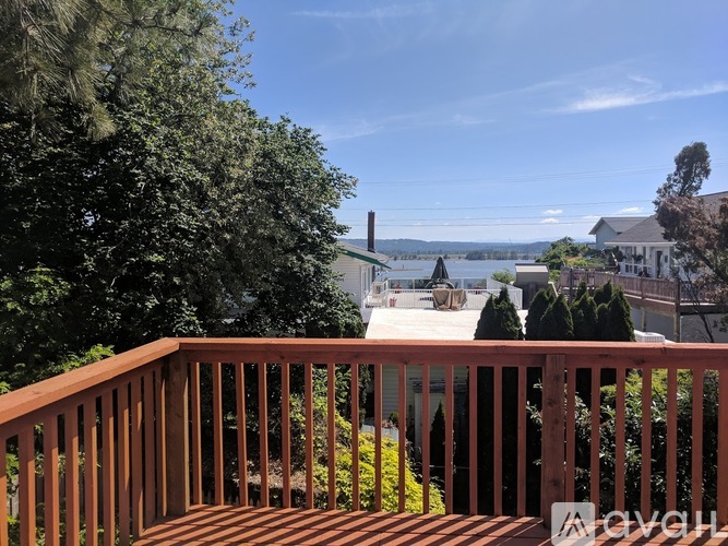 A wooden deck overlooks a body of water with houses and trees in the distance.