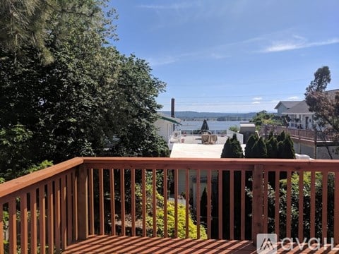 A wooden deck overlooks a body of water with houses and trees in the distance.