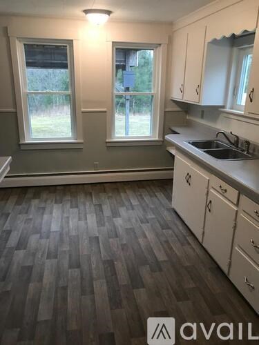 A kitchen with wooden flooring and white cabinets.