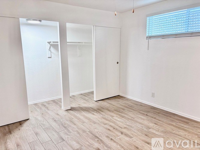 A room with a wooden floor and white walls, with a door and a window.