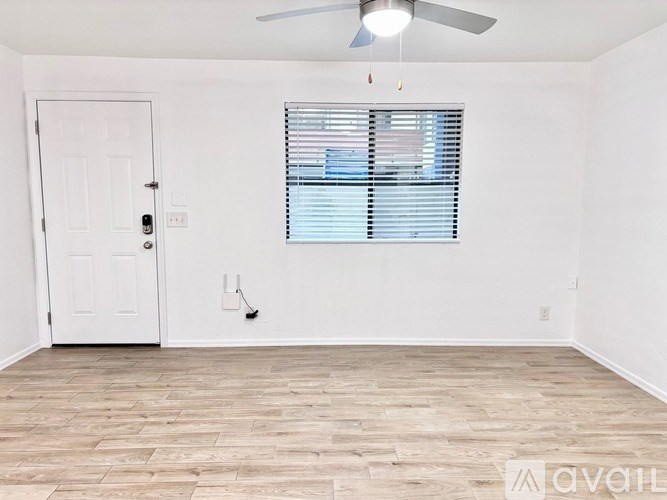 A room with a white door, a window with blinds, and a ceiling fan.
