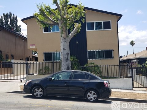 A black car is parked in front of a tan building with a tree in front of it.
