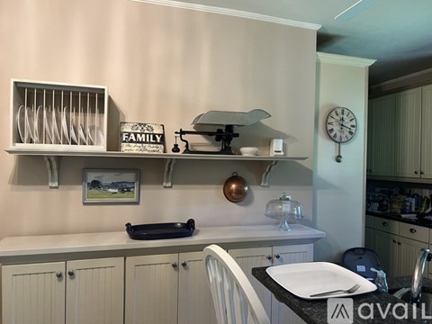 A kitchen with a white counter and cabinets, a clock on the wall, and a picture of a family on the shelf.
