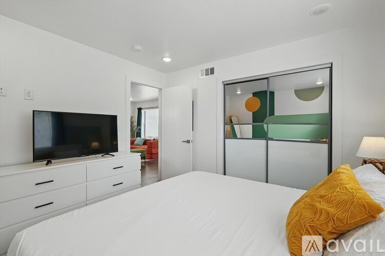 A bedroom with a bed, a television, and a mirrored closet door.