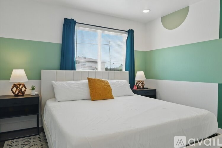 A bedroom with a white bed and a window with blue curtains.