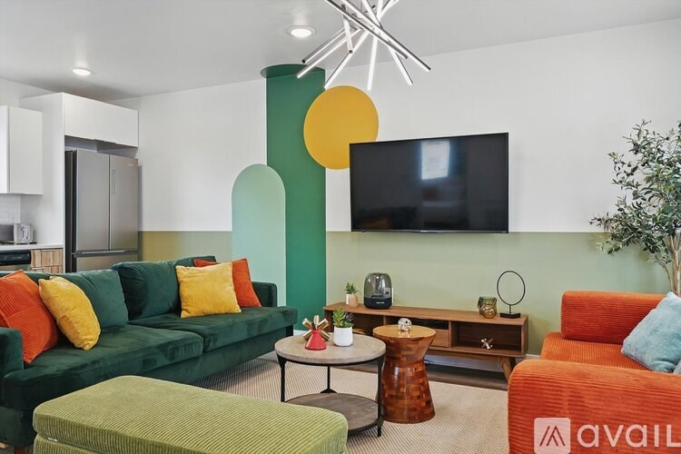 A living room with a green couch, orange chair, and a flat screen TV mounted on the wall.