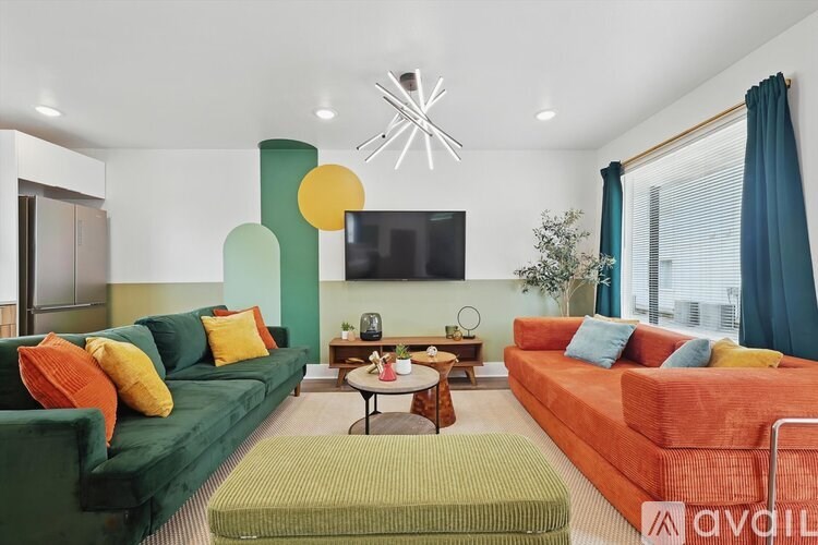 A living room with a green couch, orange couch, and a TV mounted on the wall.