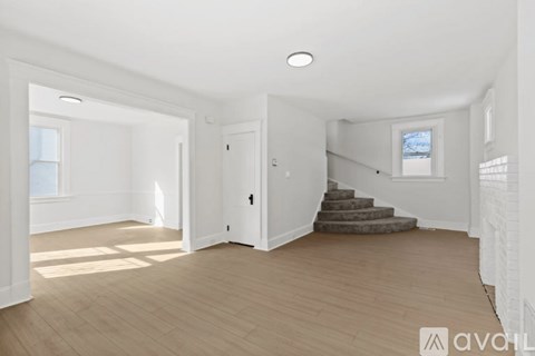 A spacious room with wooden flooring and a staircase leading to another room.
