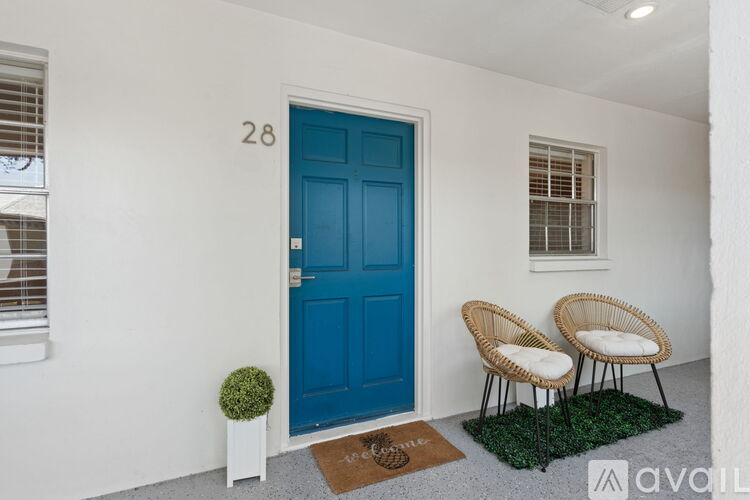 A blue door is on the left of two wicker chairs.