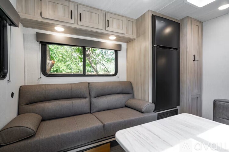 A grey couch sits in a room with a black fridge and a window.