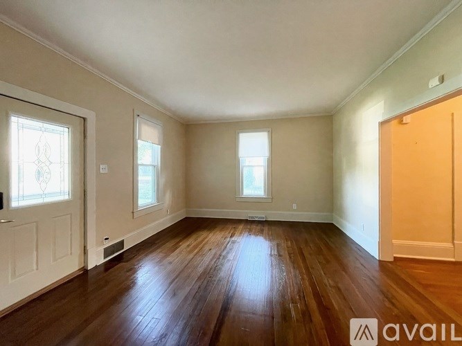 A room with wooden floors and white walls, with two windows and a door on the right side.