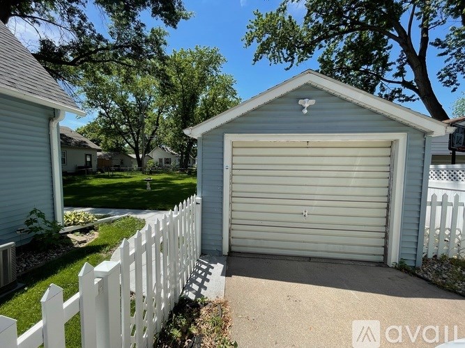 A small white house with a garage door is in front of a white picket fence.