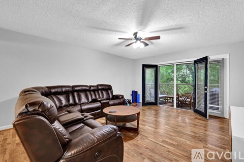 A living room with a brown leather couch and a ceiling fan.
