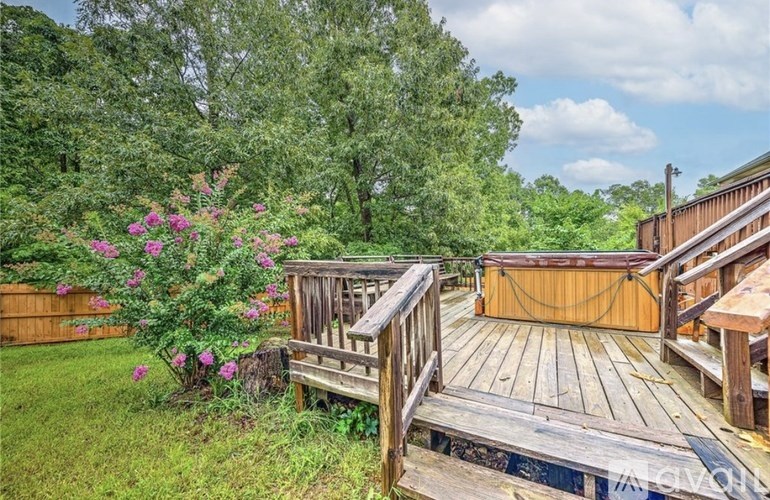 A wooden deck with a bench and a hot tub surrounded by greenery.