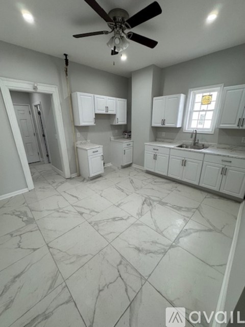 A kitchen with white cabinets and marble flooring.