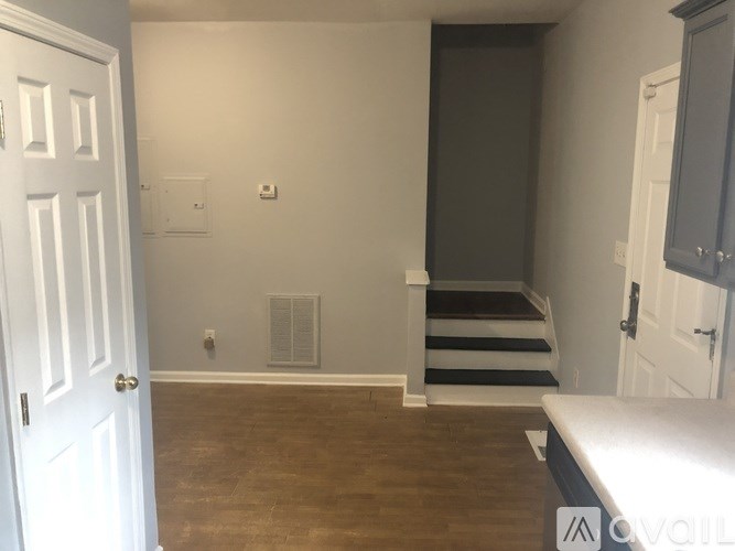 A room with a white door, a staircase, and a wooden floor.