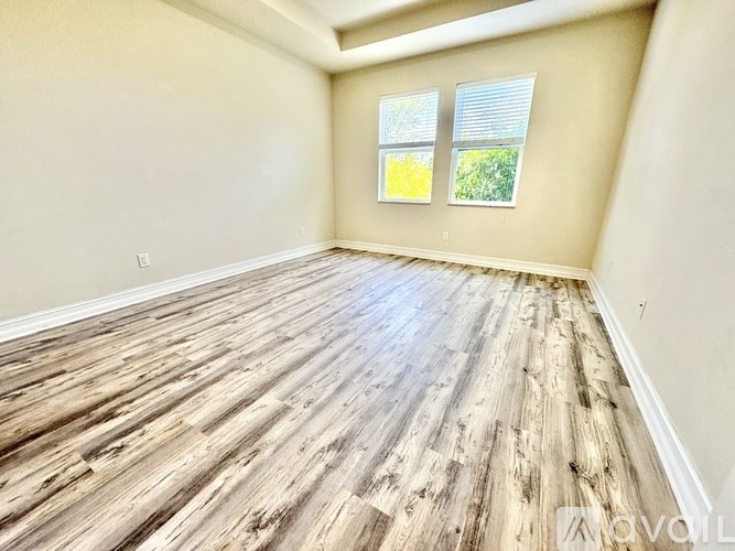 A room with wooden flooring and two windows.