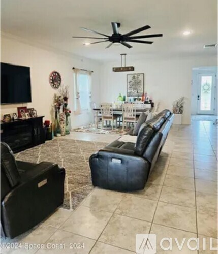 A living room with a black leather couch and a fan.