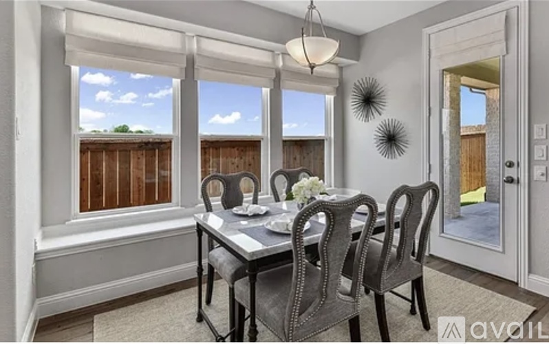 A dining room with a table set for four and a view of a wooden fence outside the window.