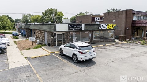 A white car is parked in a parking lot in front of a Subway restaurant.
