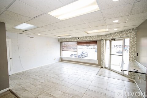 A spacious room with tiled flooring and large windows.