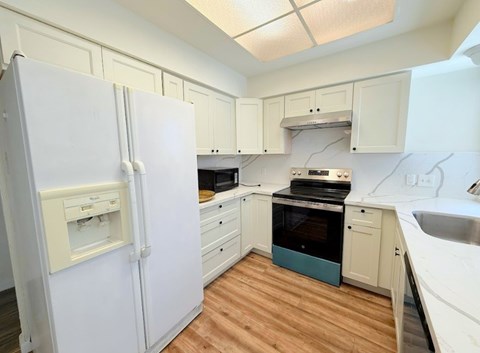A white refrigerator is in the corner of a kitchen with wooden floors.