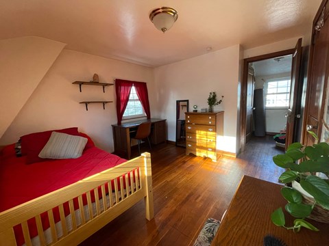 A bedroom with a red bedspread and wooden furniture.