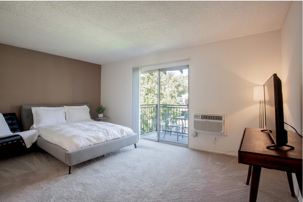A bedroom with a bed, a couch, a window, and a television.