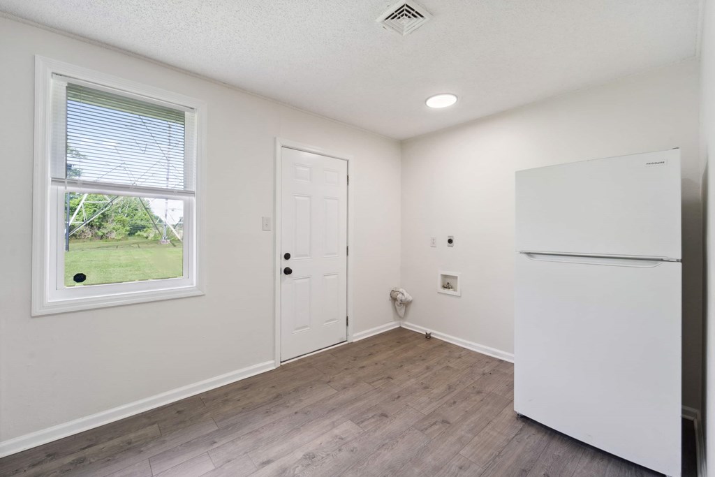 A white refrigerator sits in a kitchen with wood flooring and a window.