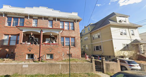 A red brick building with a balcony and a white building with a car parked in front.