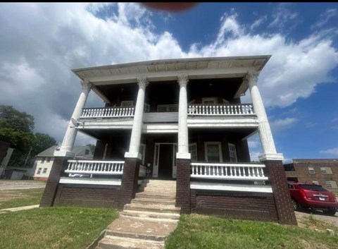 A two-story house with a white porch and a red car parked in front.