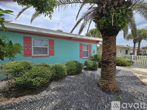 A small house with red trim and a palm tree in front.