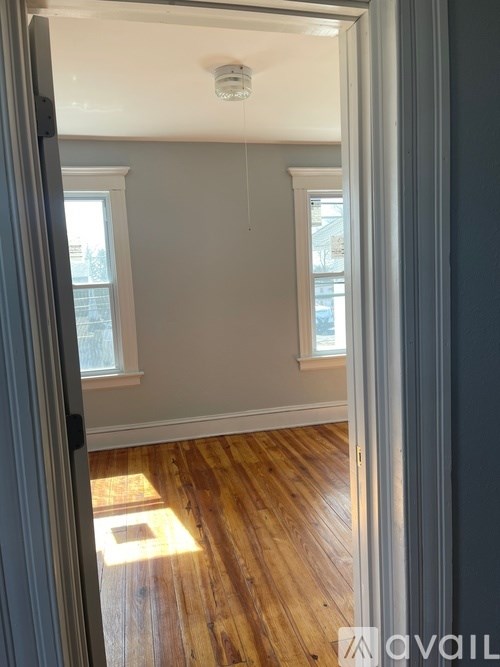 A room with wooden floors and white walls, with a window on the left side.