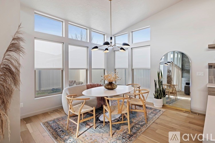 A dining room with a round table and chairs, a rug, and a large window with a view of the outside.