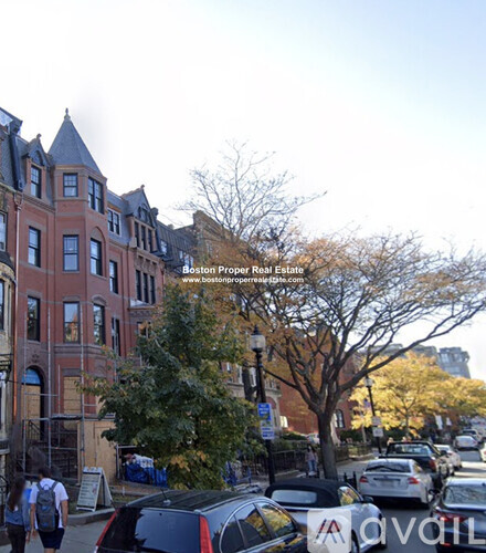 A street view of a residential area with cars parked on the side of the road and people walking on the sidewalk.
