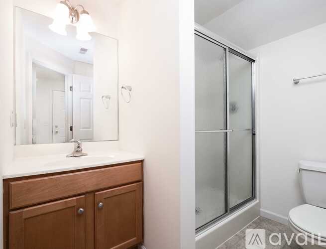 A bathroom with a white toilet, a sink with a wooden cabinet and a mirror above it.