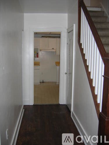 A hallway with a staircase on the right and a doorway leading to a kitchen.