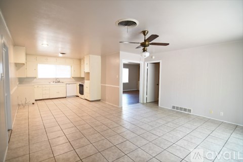 A spacious living room with a fan and a kitchen area in the background.